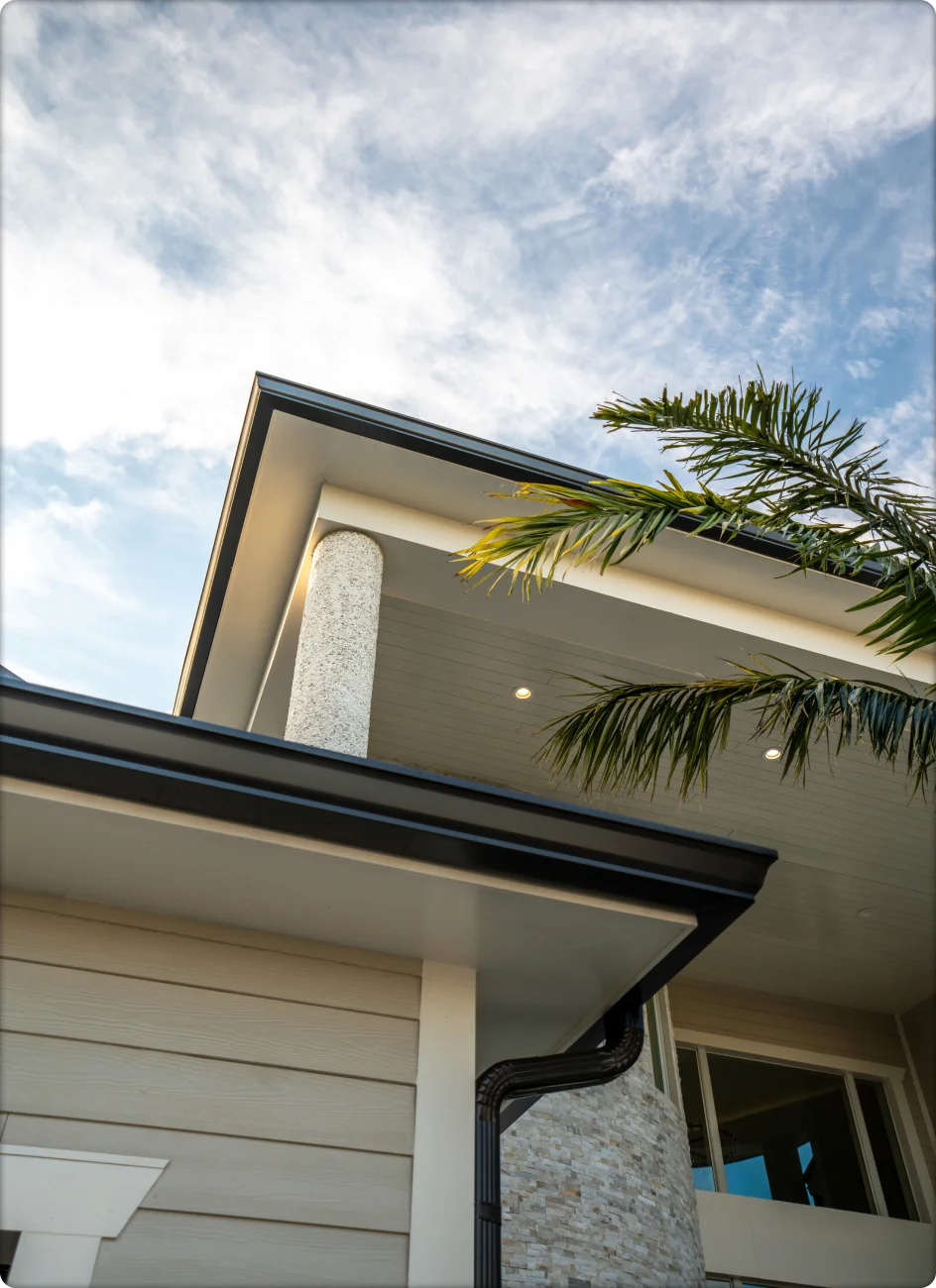 Modern home exterior with black aluminum gutters, soffit lighting, and palm tree against blue sky
