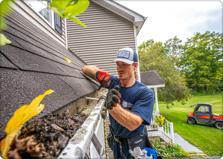 Worker using tools to clean debris from a roof gutter on a house exterior